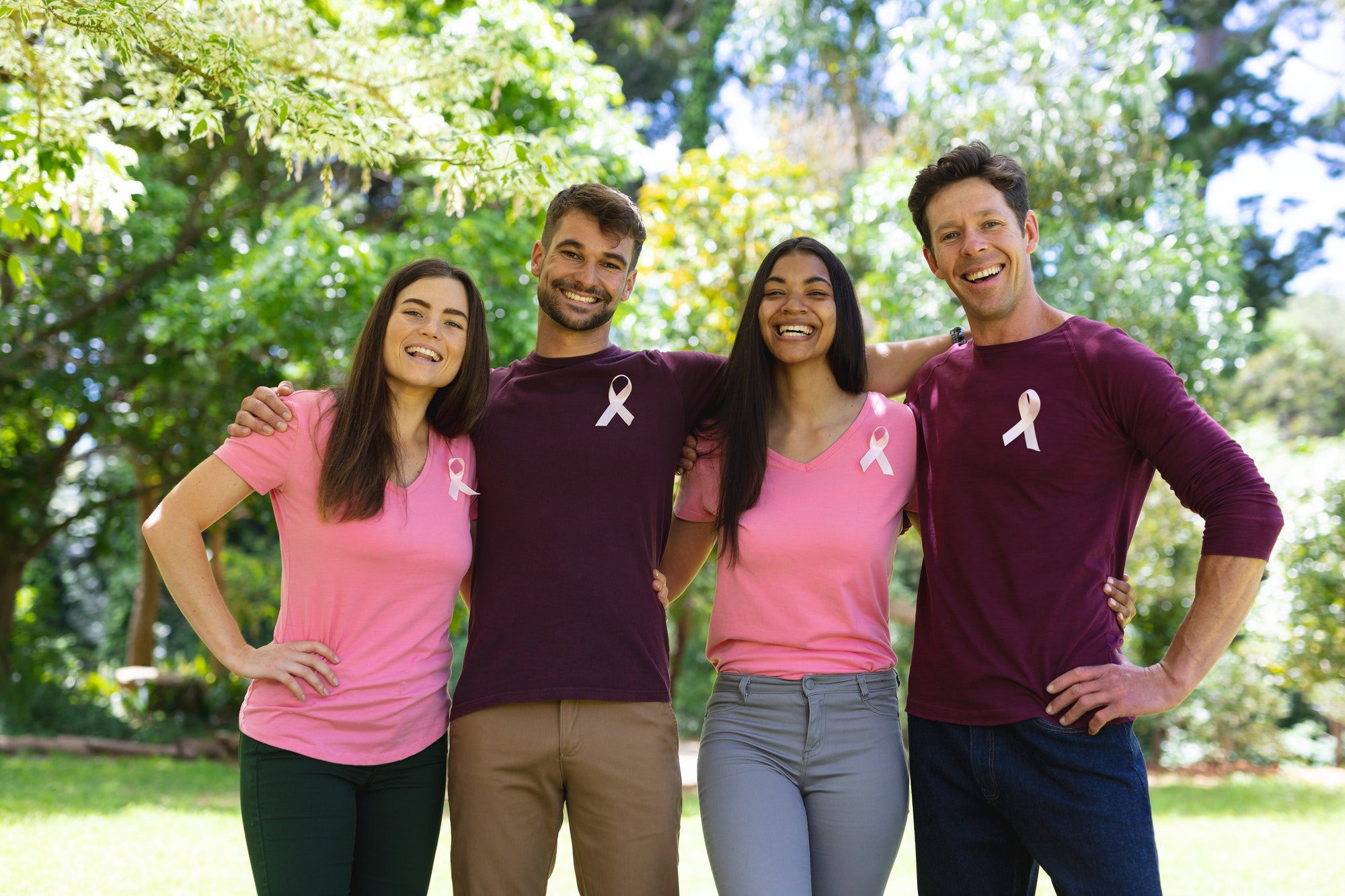 Portrait of smiling multiracial men and women wearing breast cancer awareness ribbons in park